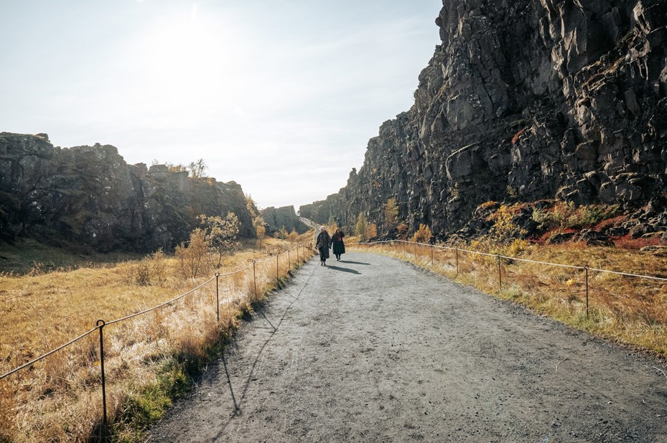 People walking on a path through rock formations at Thingvellir National Park, Iceland.