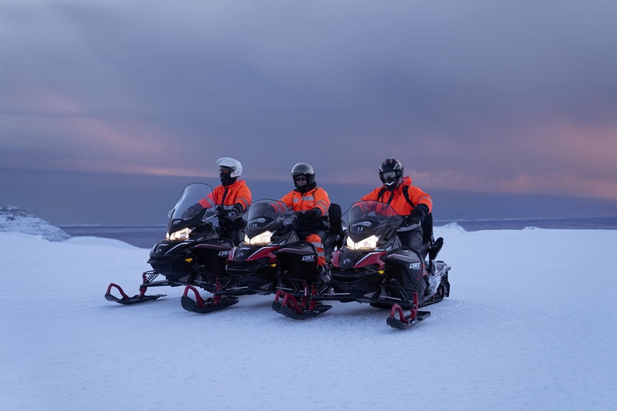 Three people riding snowmobiles on glacier