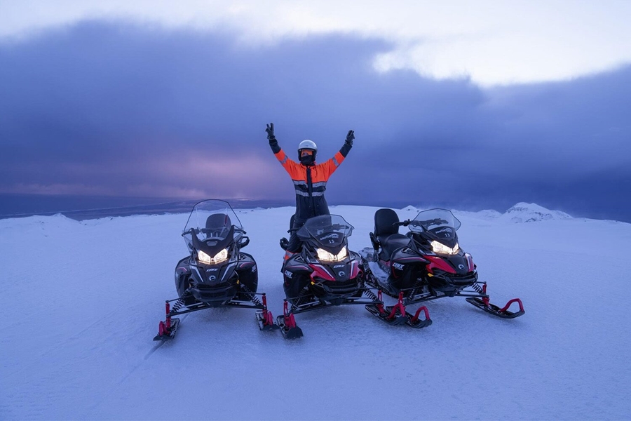 Man posing with three snowmobiles on glacier