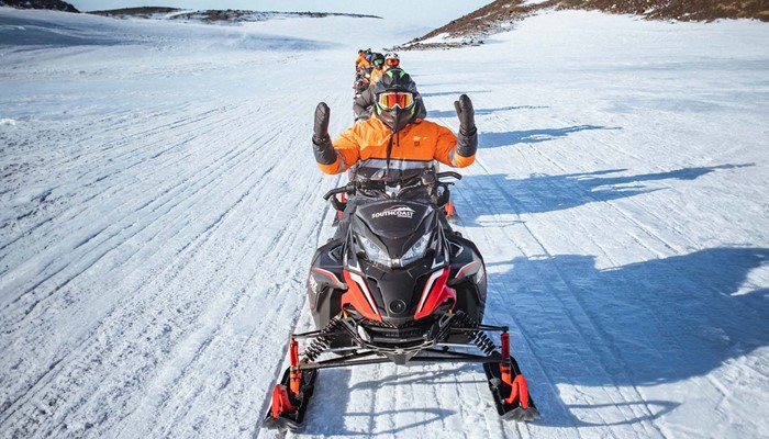 Group snowmobiling in a row on glacier