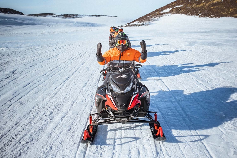 Group snowmobiling in a row on glacier