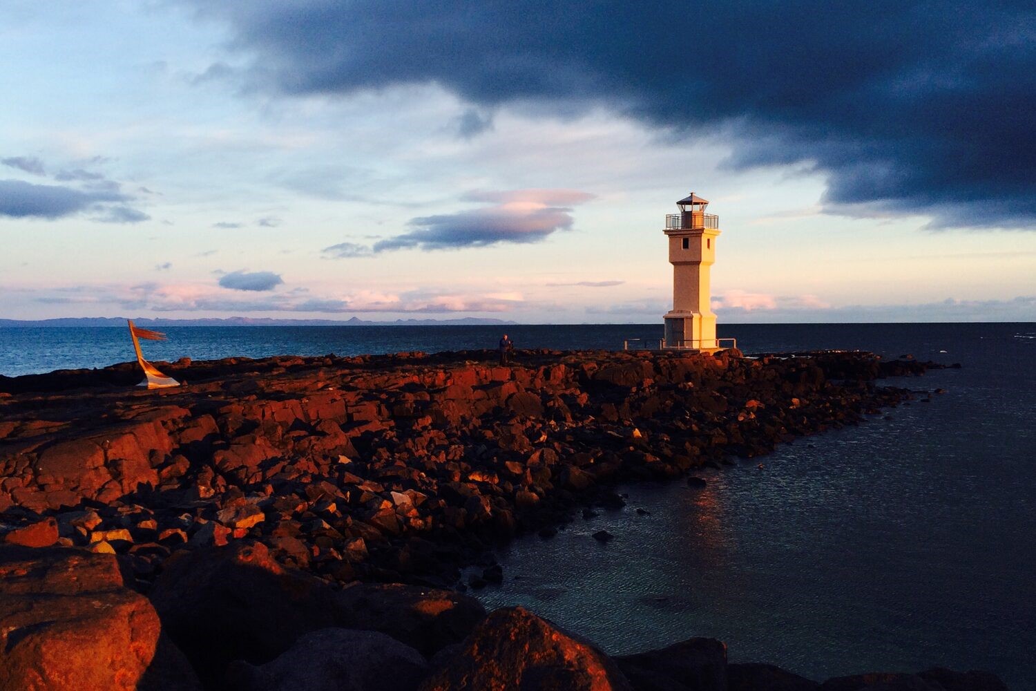 White Lighthouse in Akranes Iceland, on rocky shore by the sea with cloudy sunset 