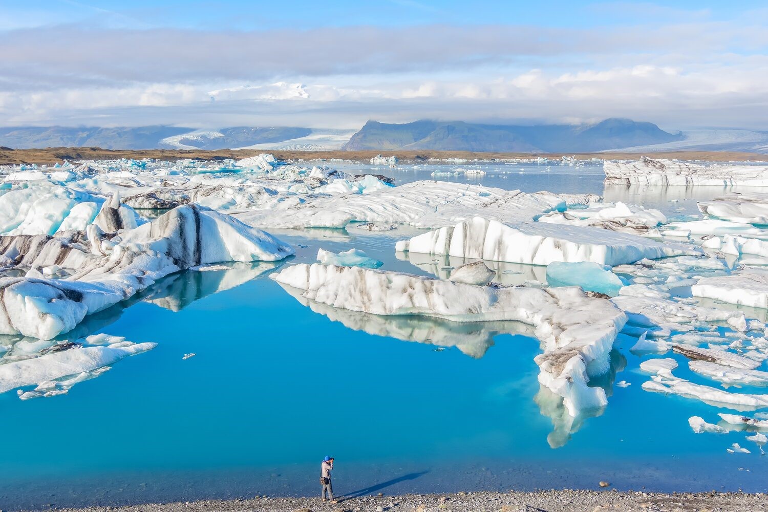 Tourist photographing Icebergs in bright blue Jokulsarlon glacial lake, Iceland with cloudy skies in background