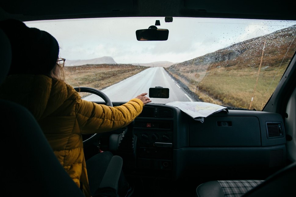 View through windshield of Woman in yellow coat driving down scenic road in Iceland