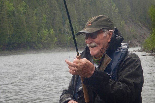 Old man close up dressed in fishing gear, with fishing rod, on river in Quebec, Canada iin the rain 