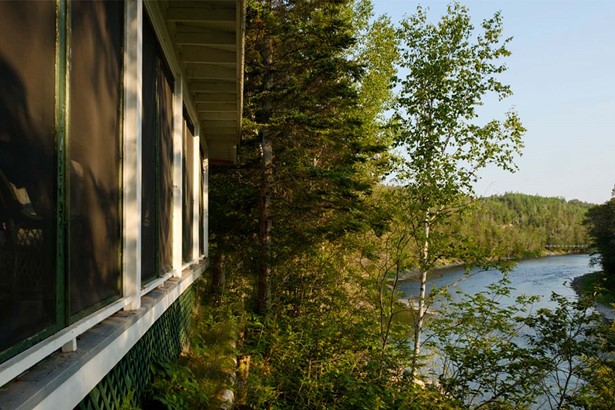 White wooden window of fishing lodge accommodation overlooking river surrounded by trees of evergreen forest