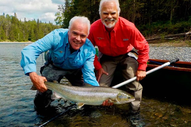 Two men with blue and red shirts posing with salmon