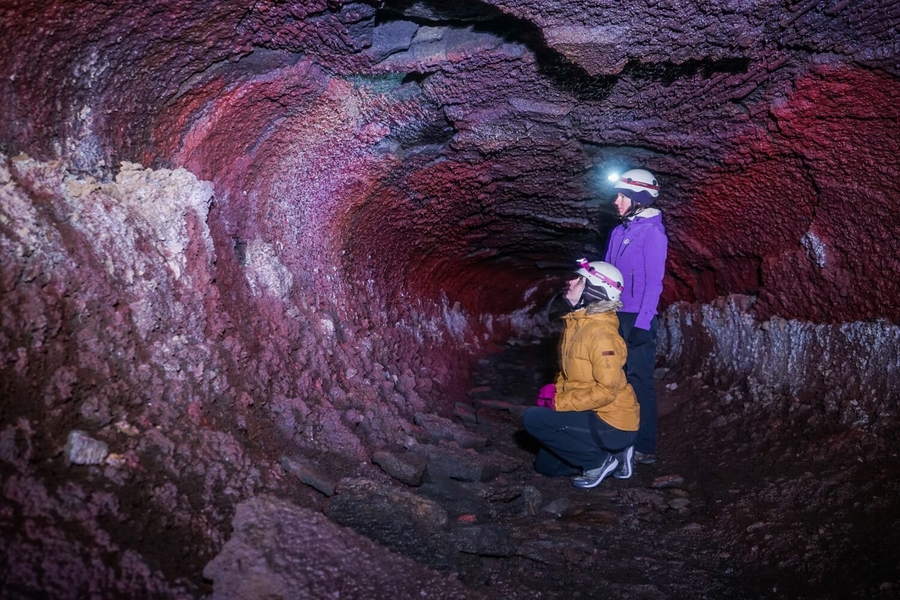 Women exploring lava tube with headlamps