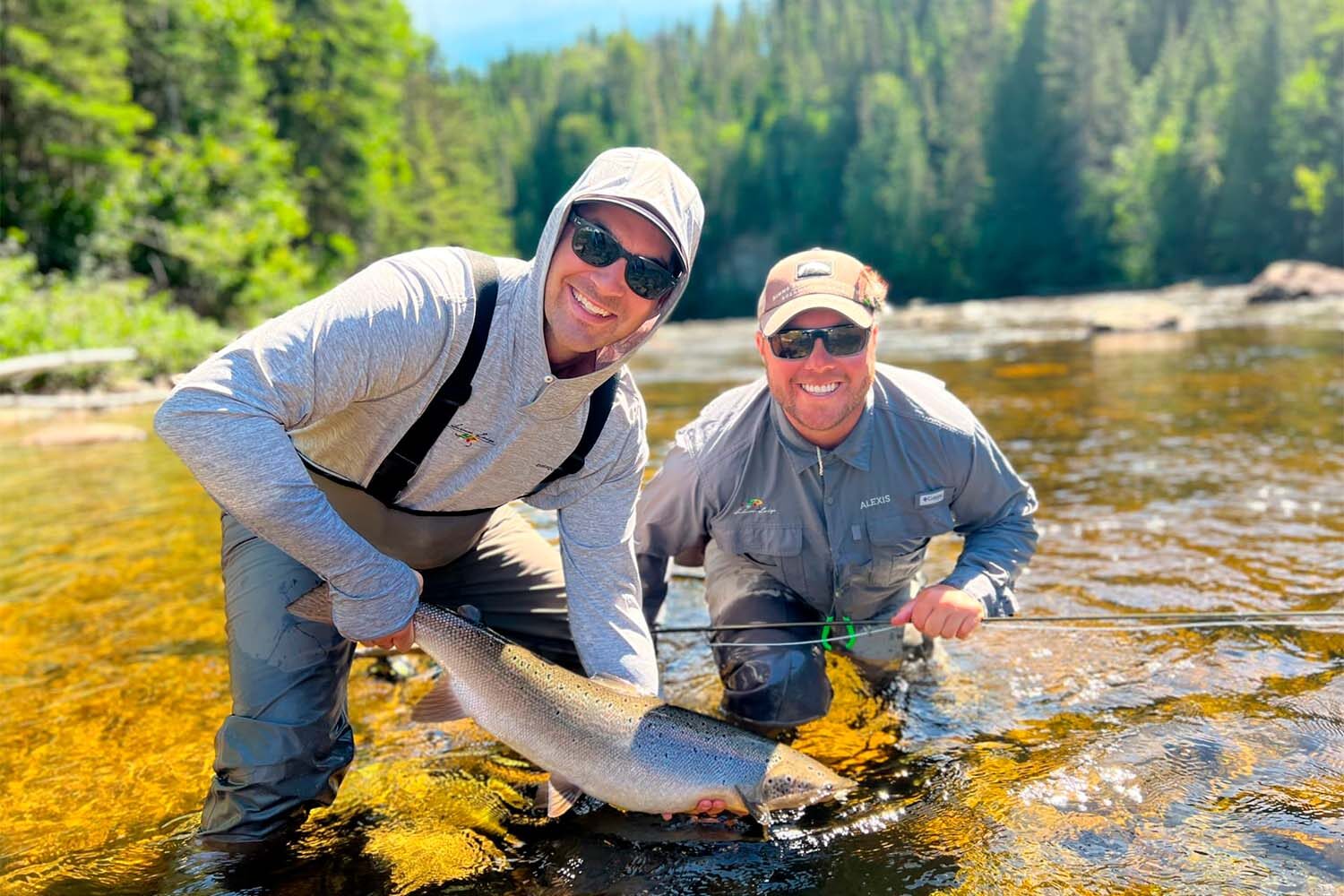 Two men in river posing for photo with salmon