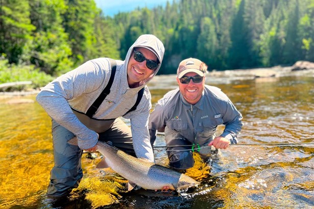 Two men in river posing for photo with salmon