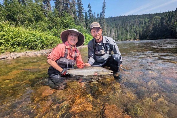 Woman and man posing for photo in river with salmon