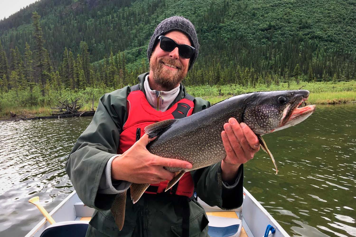 Man with red vest holding salmon by the lake in Canada