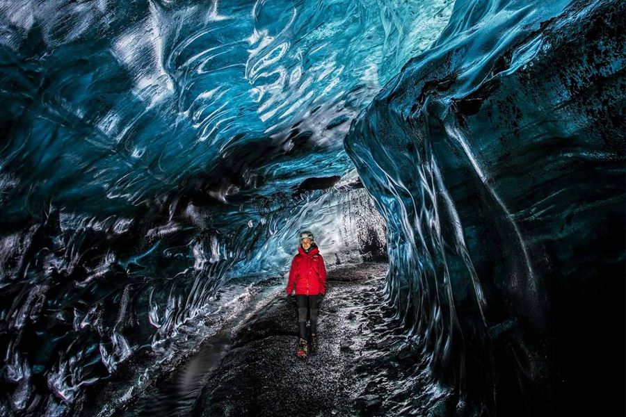 Tourists  in orange and red coat walking inside newly found crystal ice cave in Iceland.