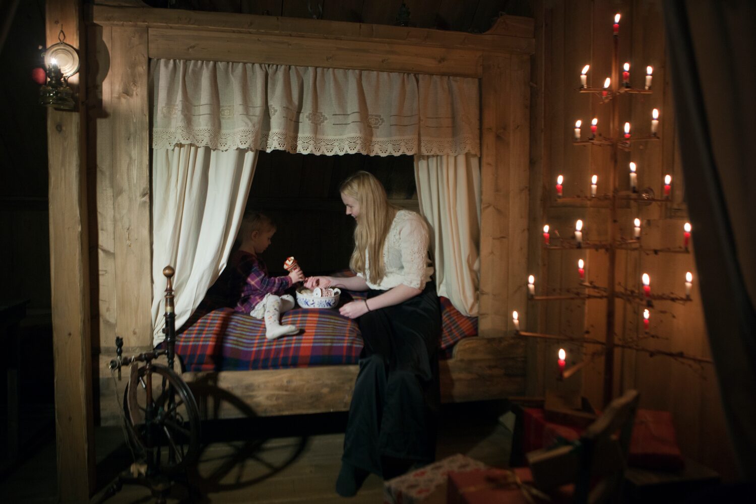 Woman sitting in bed closet with curtains and lighting in dormitory room at wilderness hotel in Iceland.