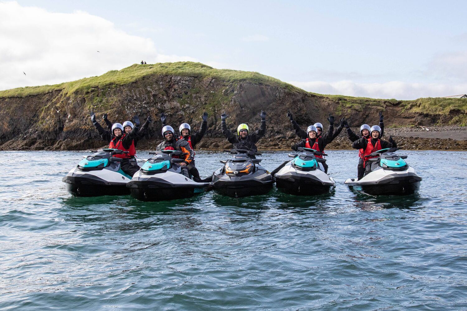 Happy group of tourists on jet skis in the sea in front of cliff in Iceland