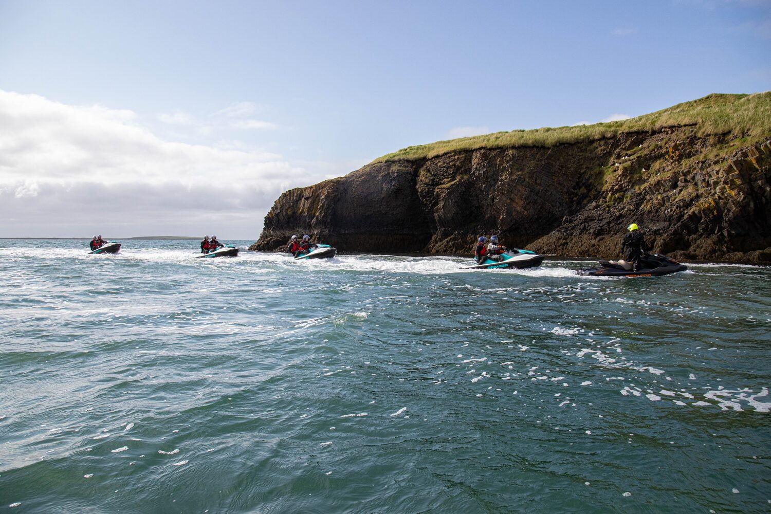 Group jet ski tour in the distance in the ocean by cliff edge