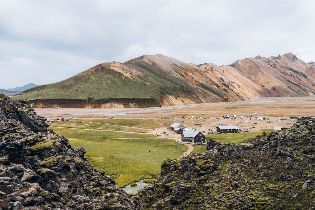 Hiking huts and people  in distance in field in front of different colored mountains 