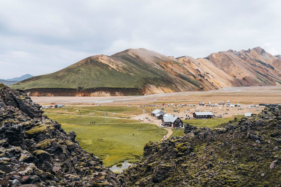 Lanmannalaugar Highlands Trail Hiking huts and people  in distance in field in front of different colored mountains