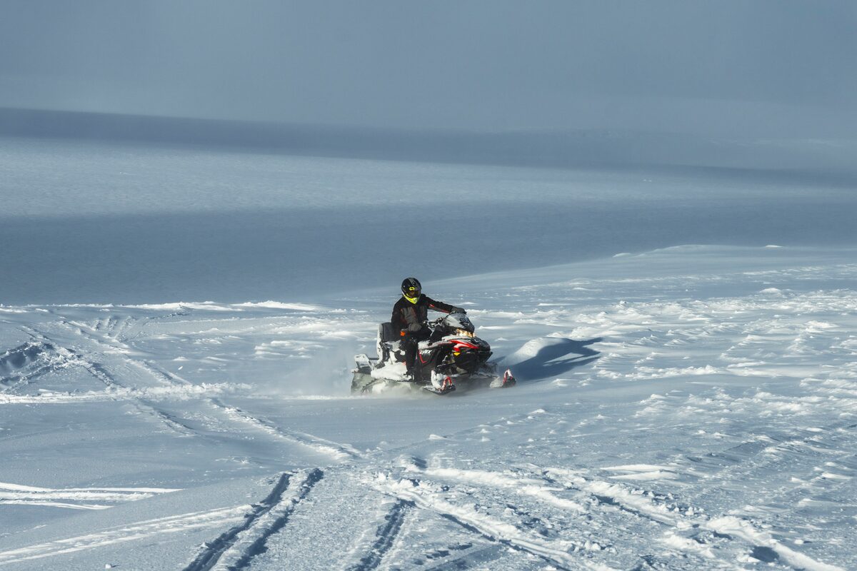 Snowmobiler driving across Langjokull glacier leaving tracks on snow 