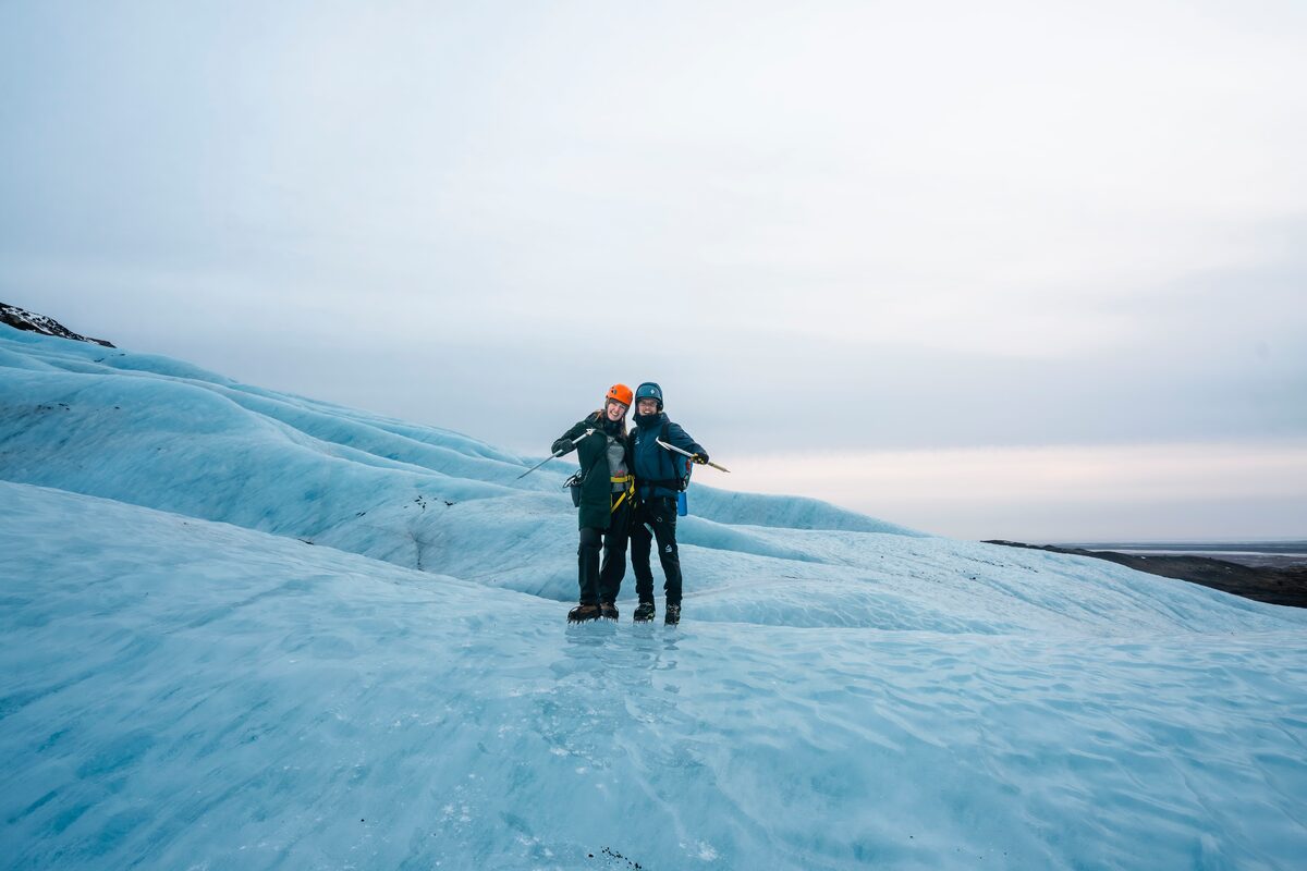 Couple posing for photo standing on blue glacier floor holding ice picks