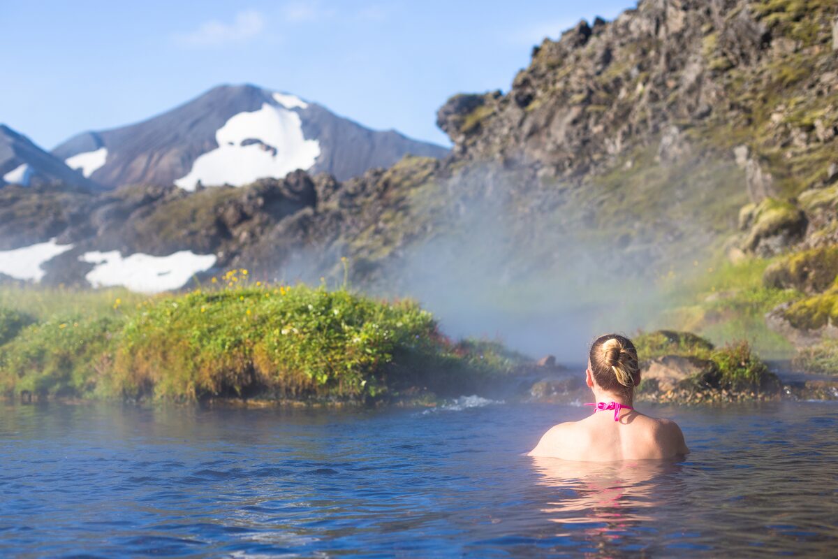 View of back of female tourist bathing in hot springs Landmannalaugar