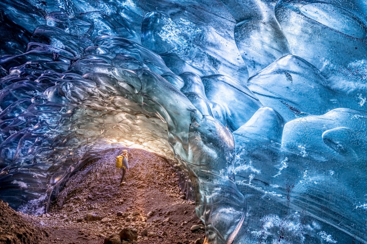 Female tourist admiring light shining through blue crystal ice cave