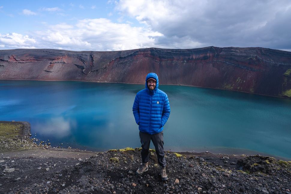 Tourist in blue jacket standing posing for photo in front of deep blue lake