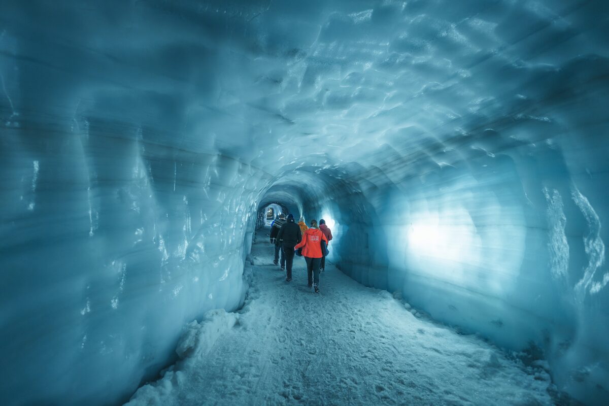 Small group walking through ice tunnel with blue crystal like walls 