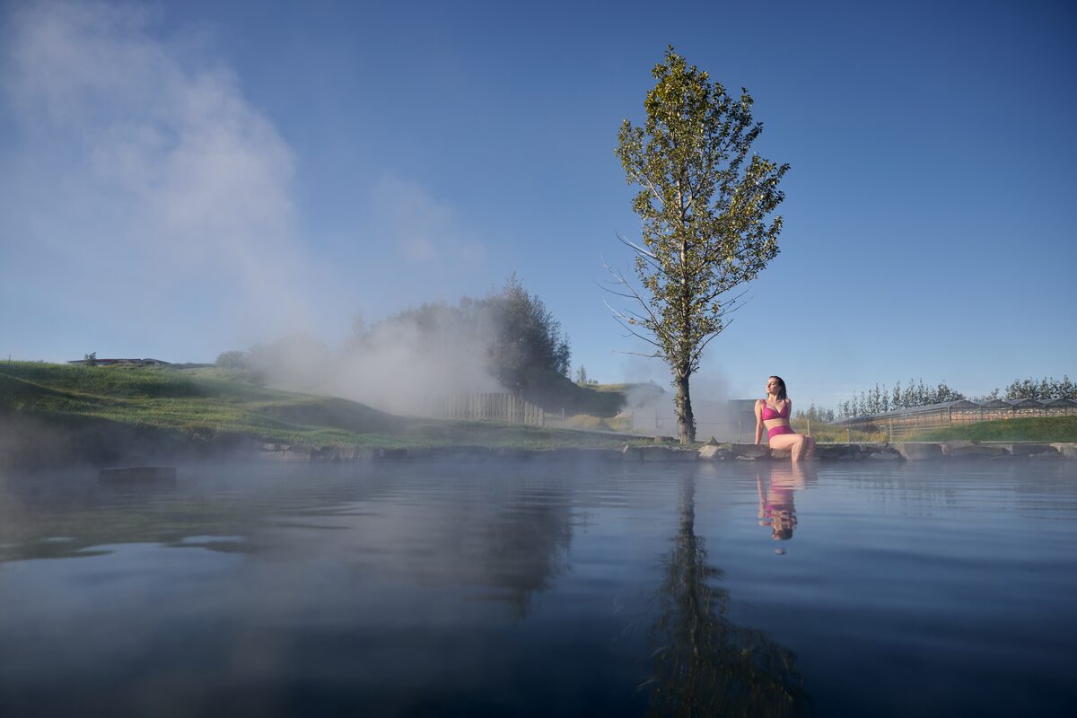 Female sitting on edge of secret lagoon pool dipping toes in pool