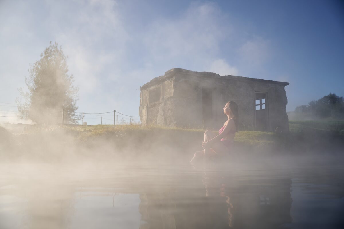 Steamy secret lagoon with lady relaxing on bank next to pool