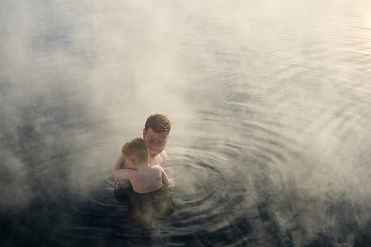 Sun down reflecting on geothermal pool with father and child bathing