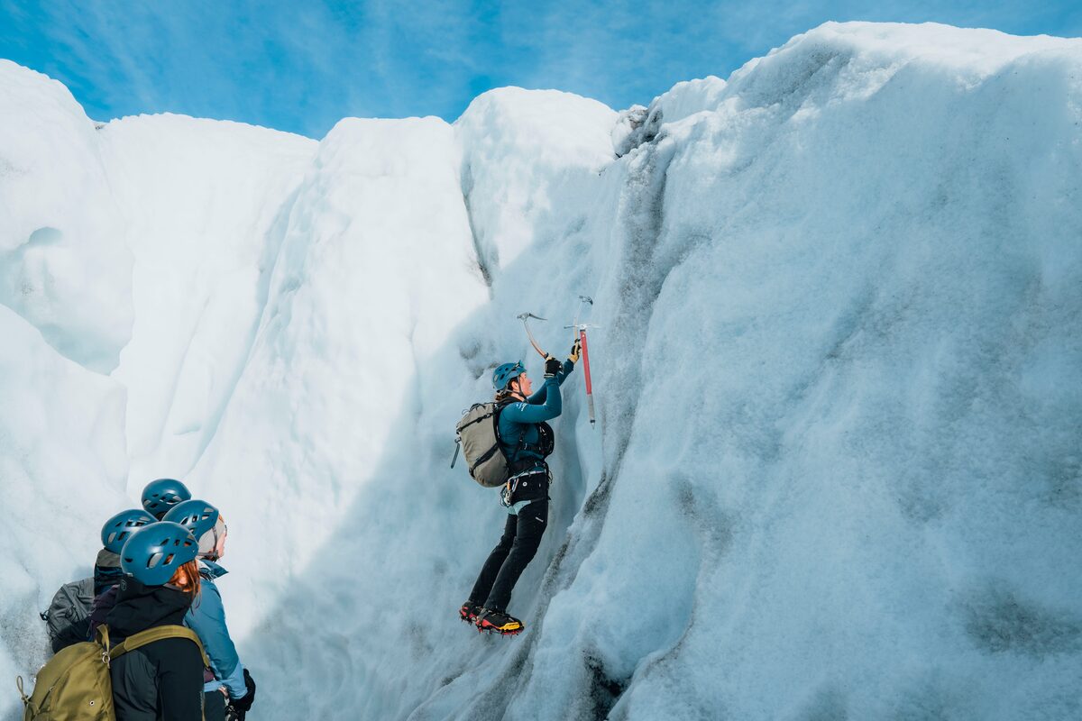Glacier guide and tourist climbing glacier ice crevasse in Iceland,