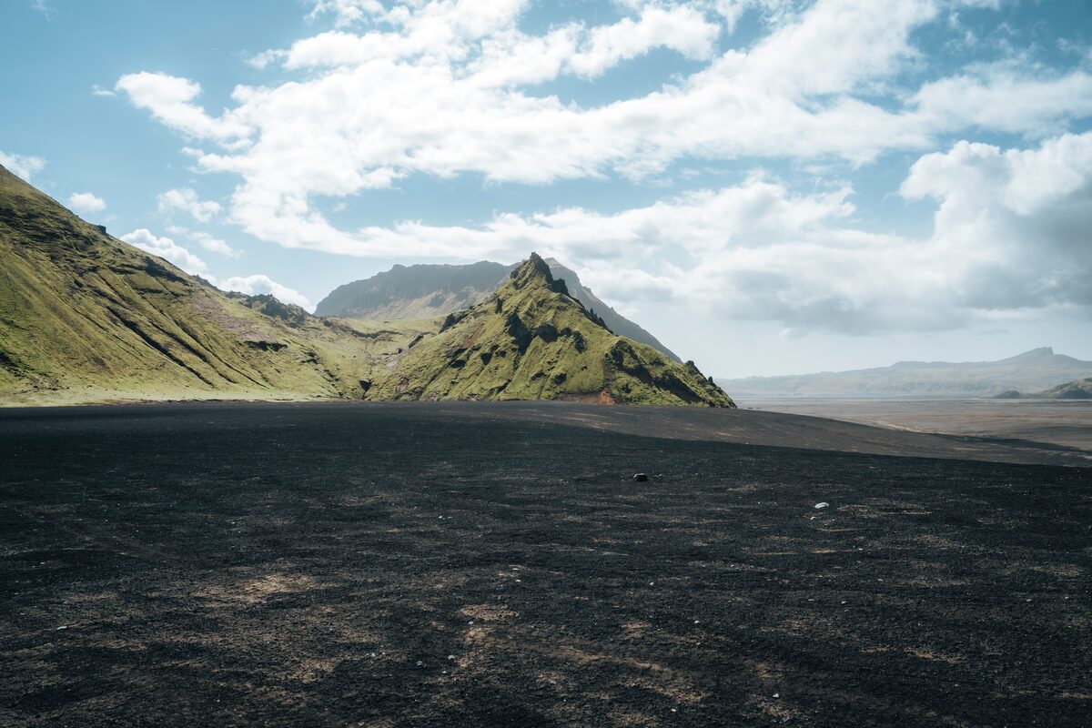 Katla Volcano partially covered in vibrant green moss, with dark volcanic rock formations and misty clouds hovering above the rugged Icelandic landscape.