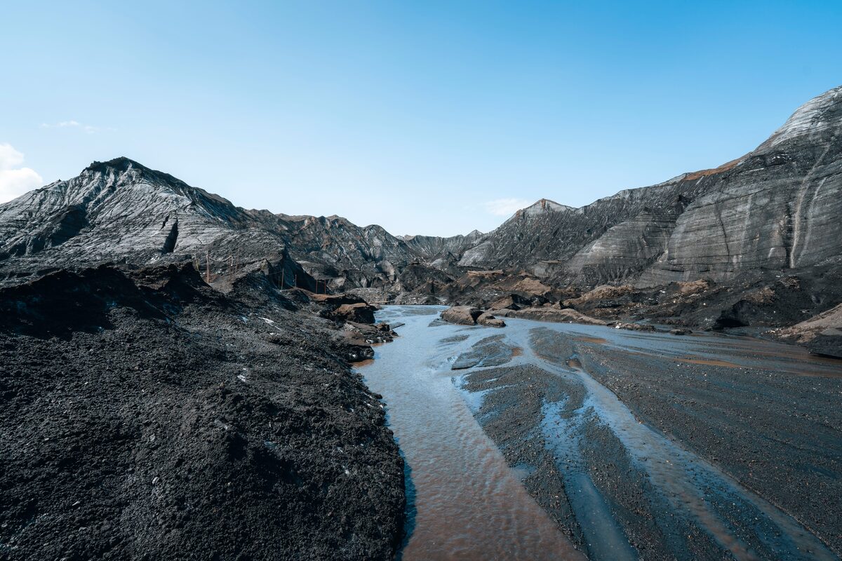 Scenic view of the Katla Volcano surroundings with winding glacial streams cutting through black volcanic sand and moss-covered terrain under a cloudy sky in Iceland.