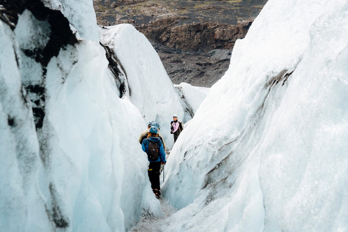 Hiker trekking through deep blue crevasses on a glacier in Skaftafell, Iceland, surrounded by towering ice walls and rugged terrain.