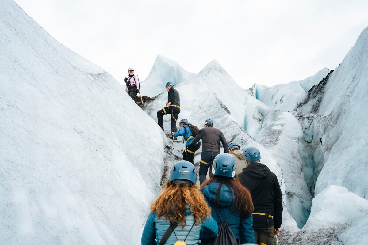 A group of hikers climbing upward on a glacier in Skaftafell, carefully navigating between crevasses with ice axes and crampons amid rugged, icy terrain.