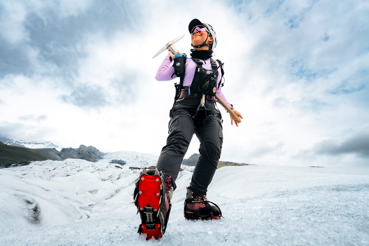 Woman wearing ice shoes wielding ice pick axe and safety helmet, for glacier hiking exploration on Skaftafell.