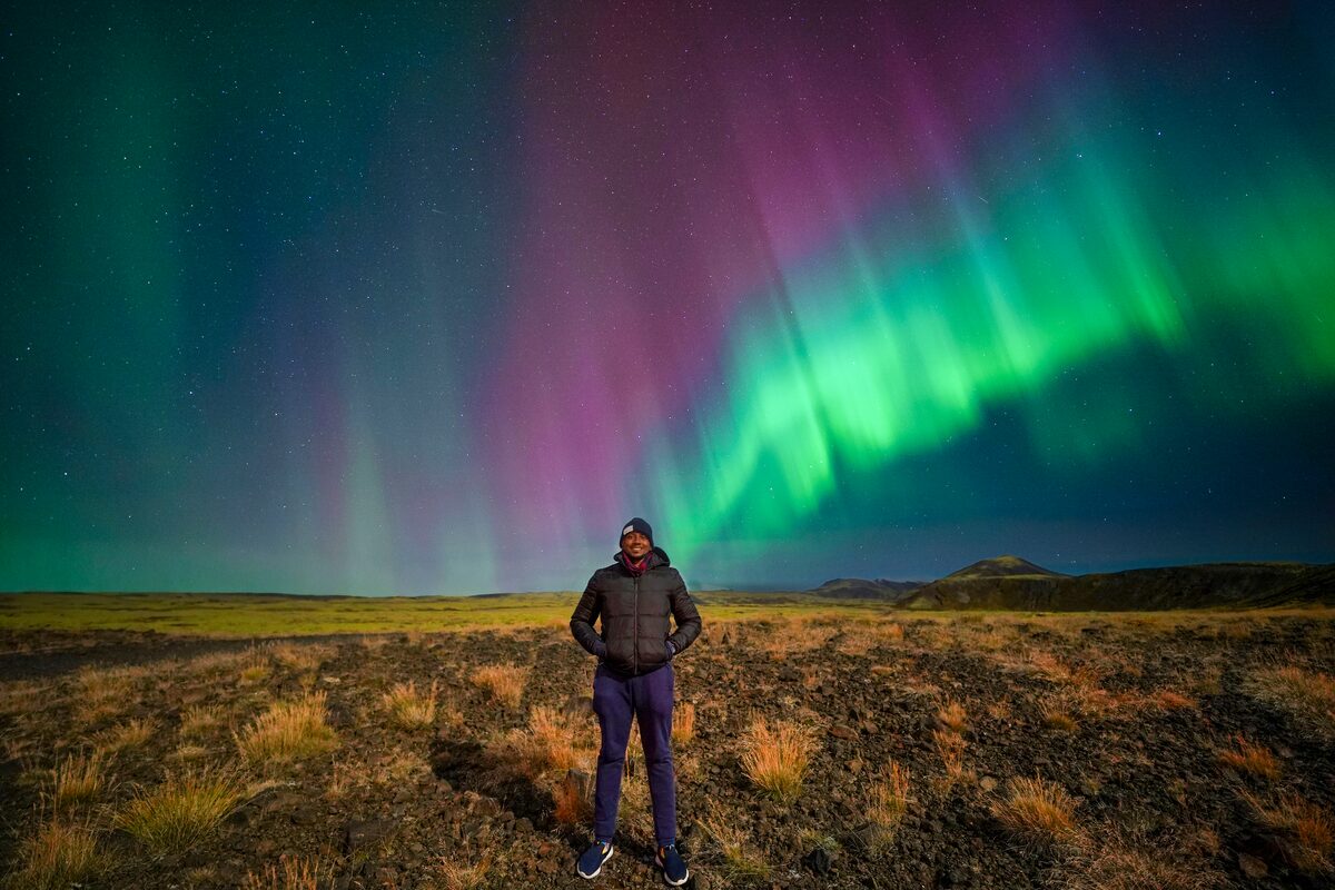 Male tourist posing underneath Aurora Borealis at lava field in South West Iceland.