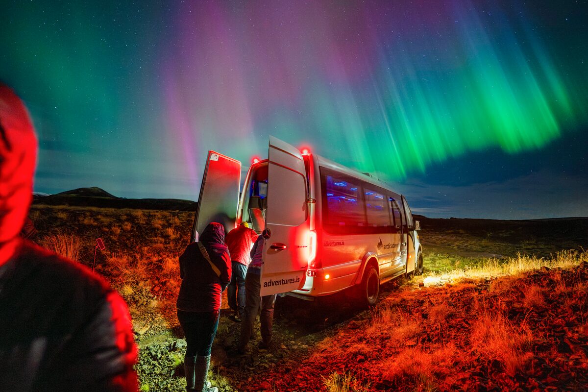 Tourists climbing up to Arctic Adventures tour bus during bright show of northern lights in Iceland.
