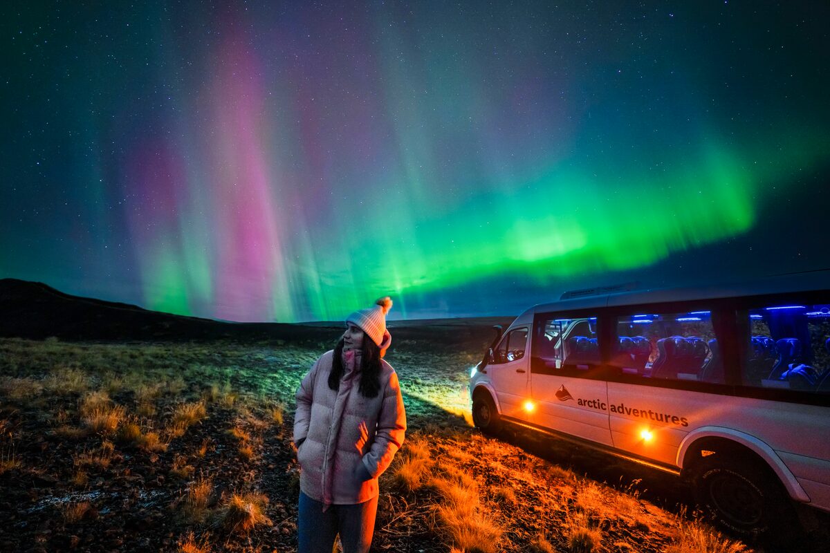 Female posing underneath bright show of northern lights in south west Iceland in autumn.