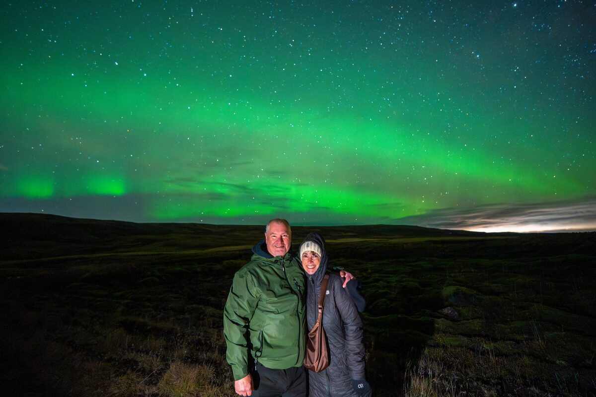 Couple hugging and posing for photo underneath green northern lights in Iceland.