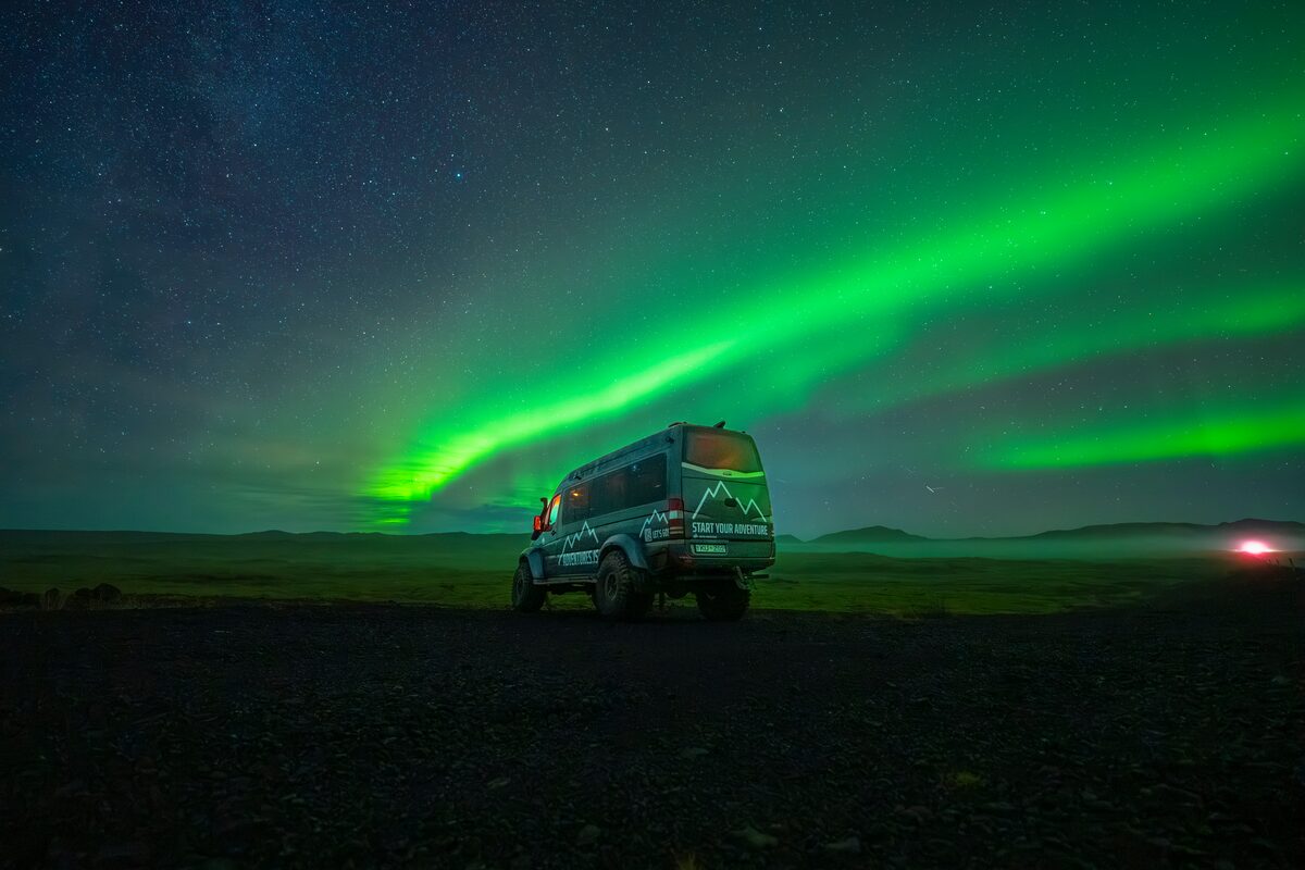 Adventures super jeep driving underneath bright green aurora borealis in Iceland.