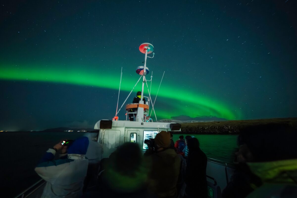 Small group tour standing around interior boat deck, viewing green northern lights by Reykjavik sea.