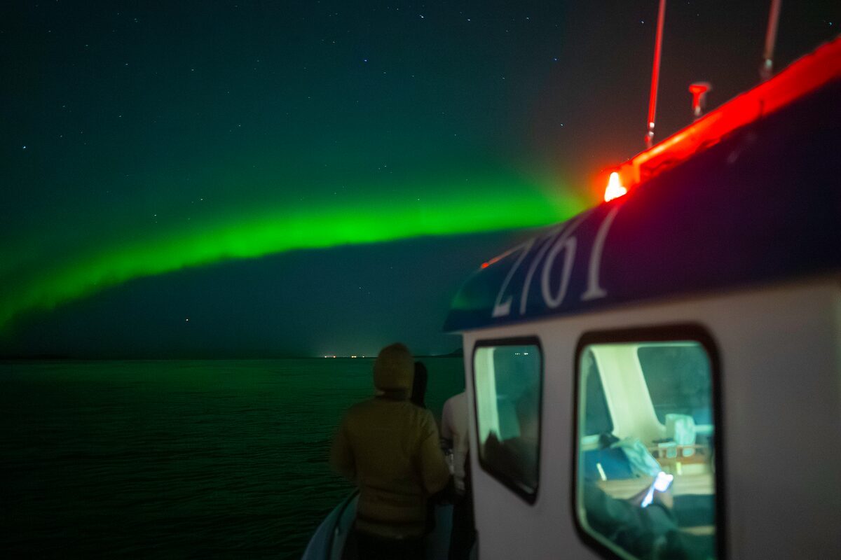 Tourist watching northern lights by boat deck in Reykjavik ocean.