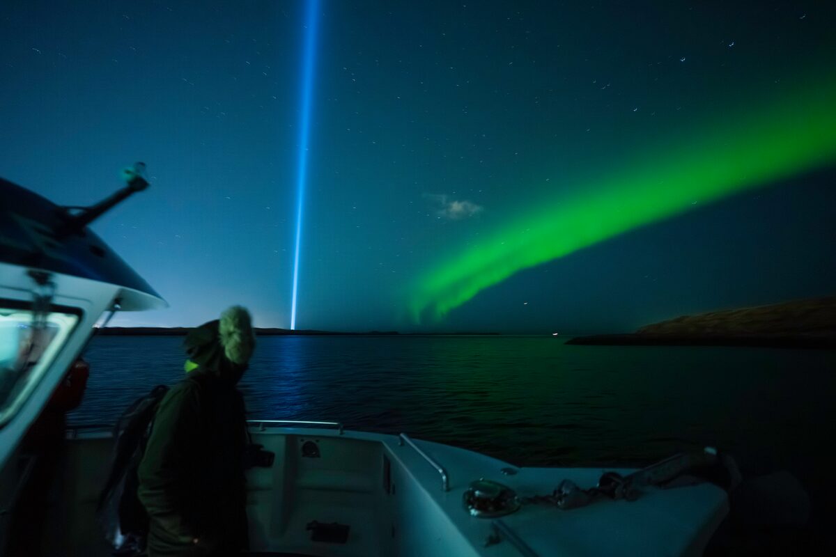 Tourist in winter jacket watching over northern lights from boat in Reykjavik Iceland.