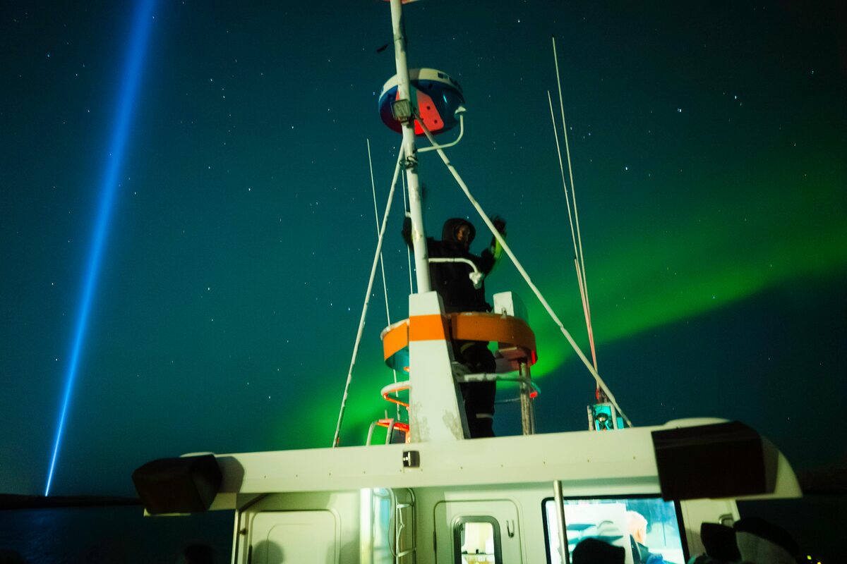 Tourist stnading in boat crows nest, viewing the green northern lights in Reykjavik's ocean.