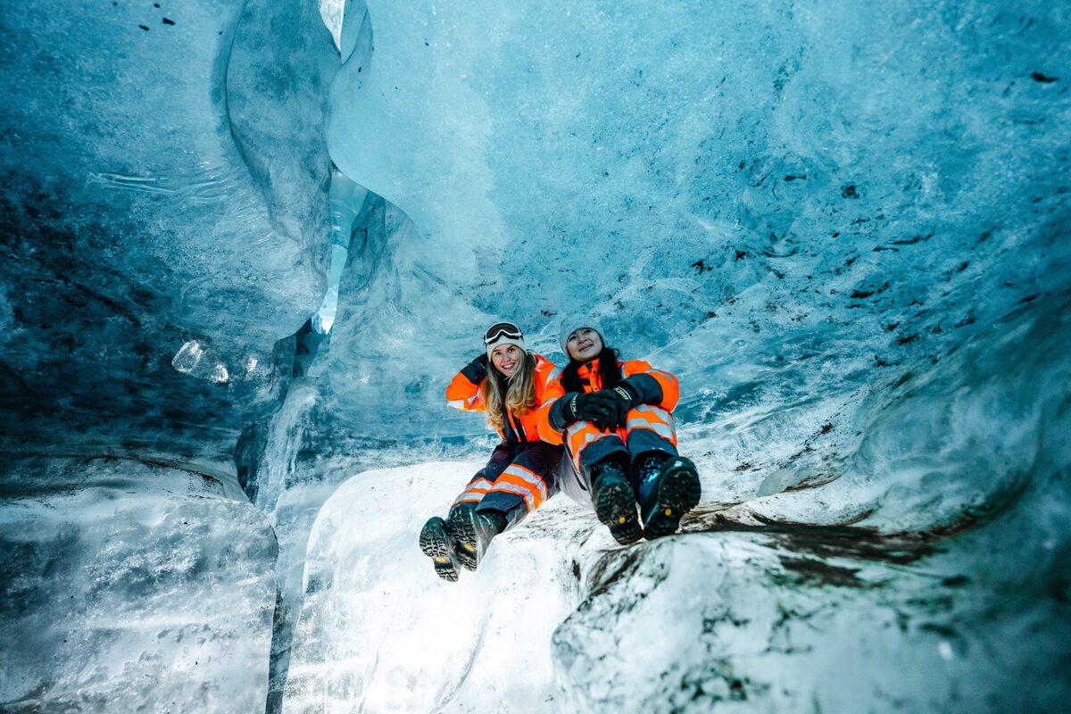 Two Women Sitting Inside Of An Ice Cave In Iceland