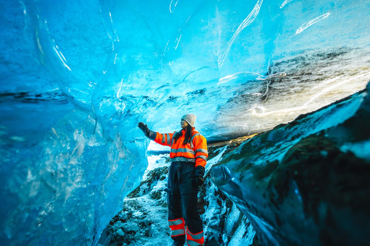 Woman In Snowmobiling Gear Touching A Wall Of An Ice Cave in iceland