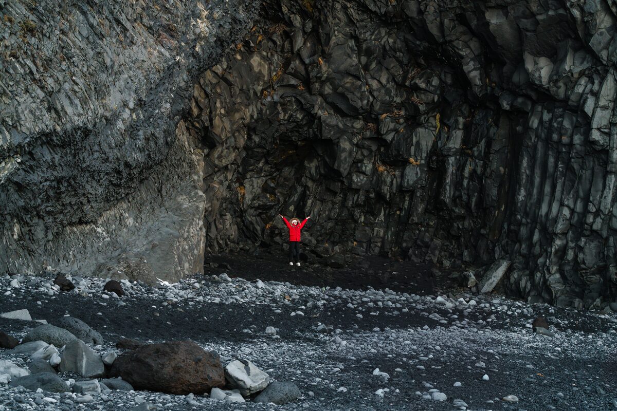 Man In A Cave On A Black Sand Beach In Iceland with basalt columns