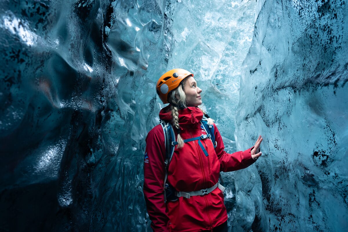 Woman In A Red Coat Touching Walls Of Crystal Ice Cave in iceland